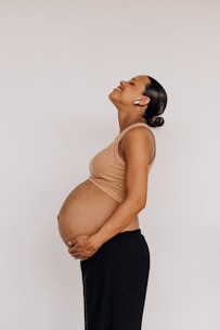 a pregnant woman in black pants and a tan tank top