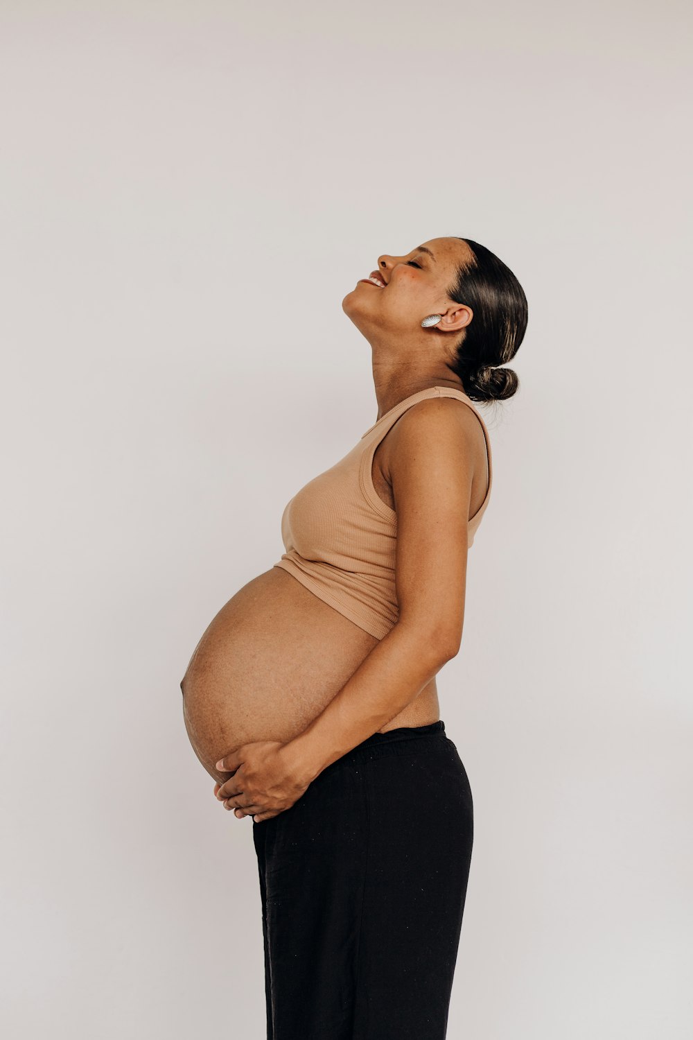 a pregnant woman in black pants and a tan tank top