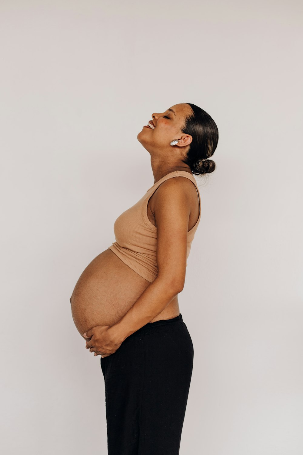 a pregnant woman in black pants and a tan tank top