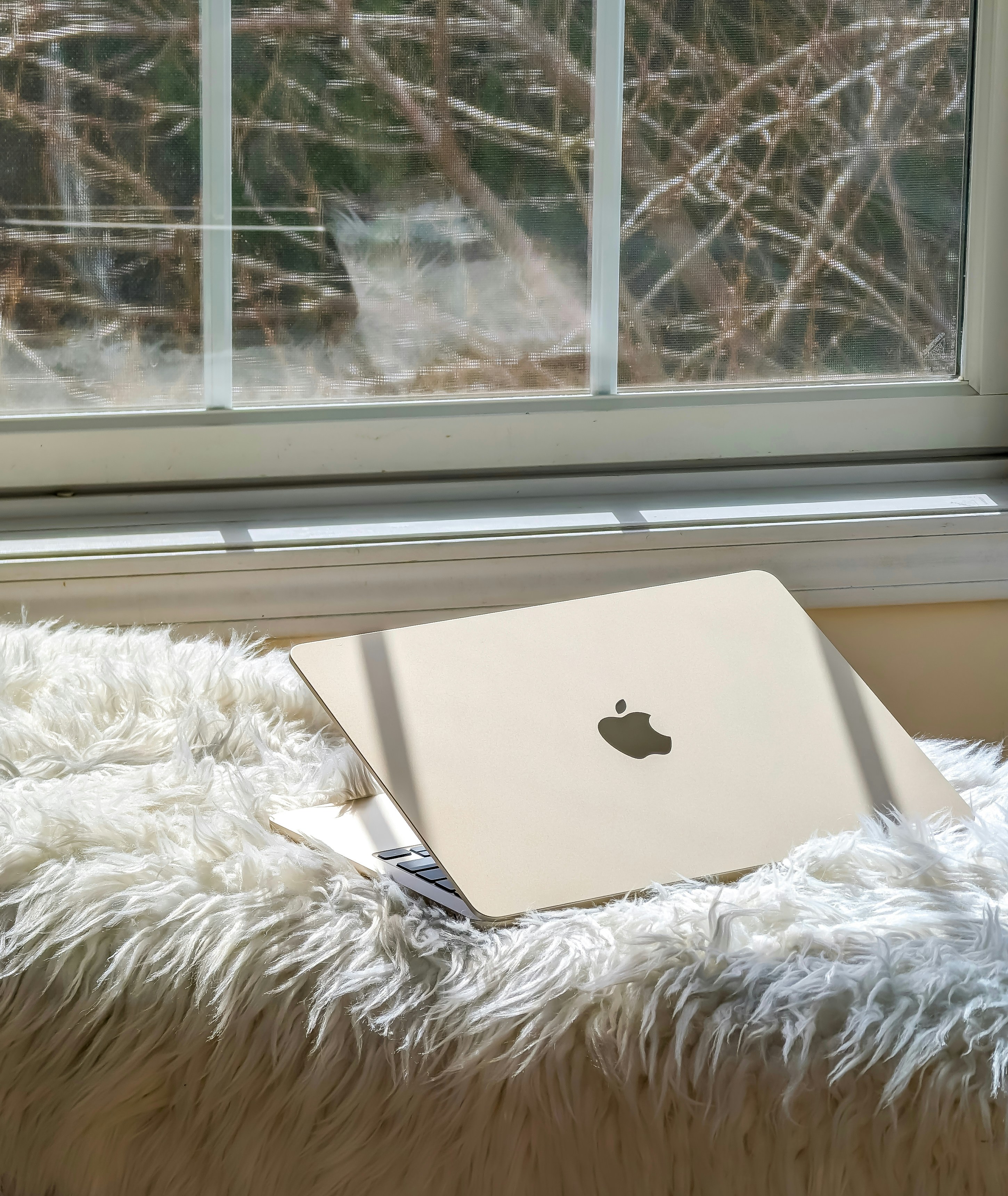 an apple laptop sitting on a fluffy blanket in front of a window