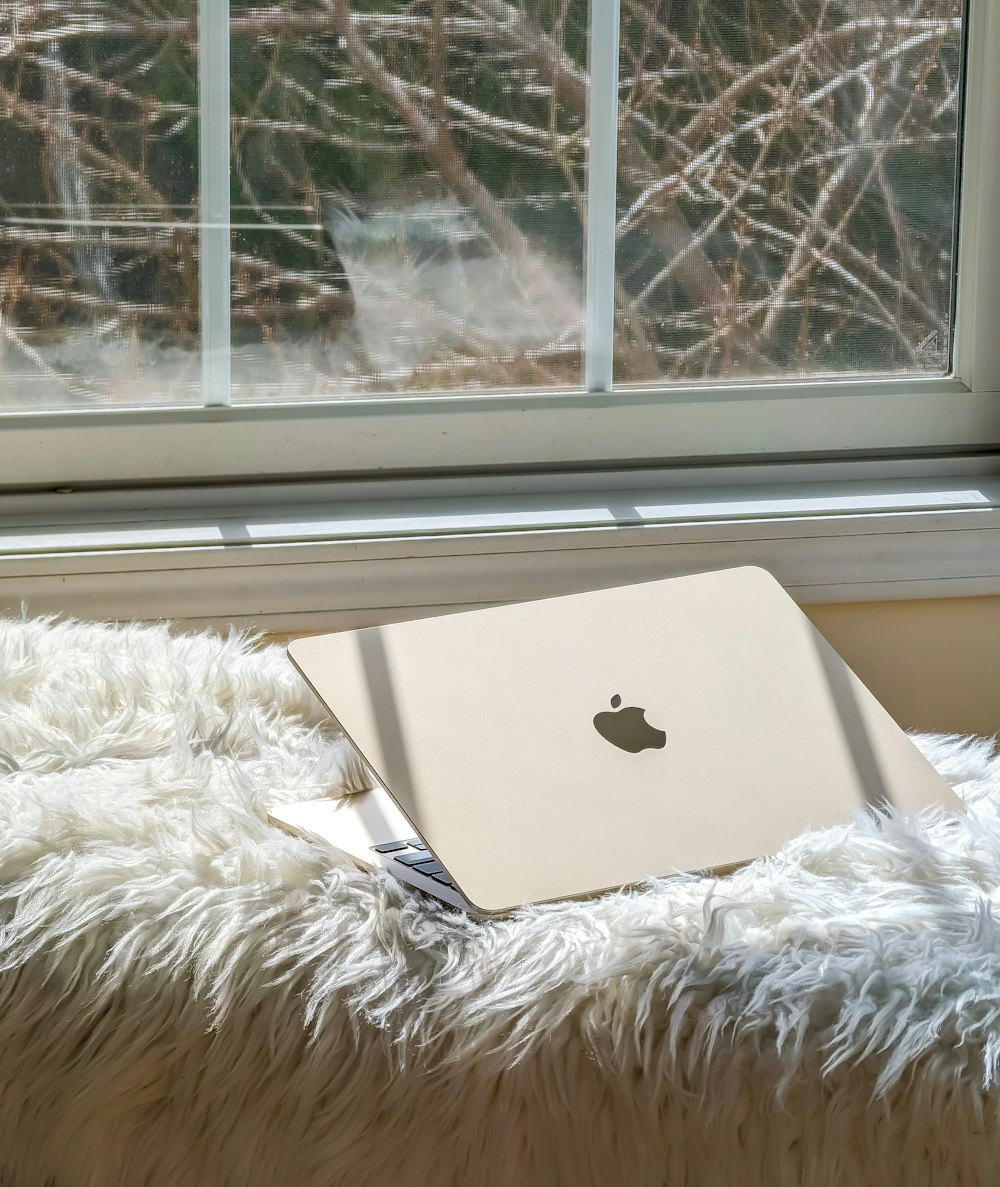 窓の前のふわふわの毛布の上に置かれたアップルのノートパソコン