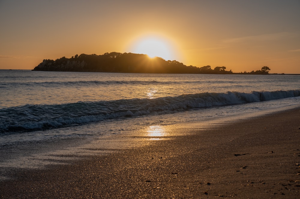 the sun is setting over the water at the beach