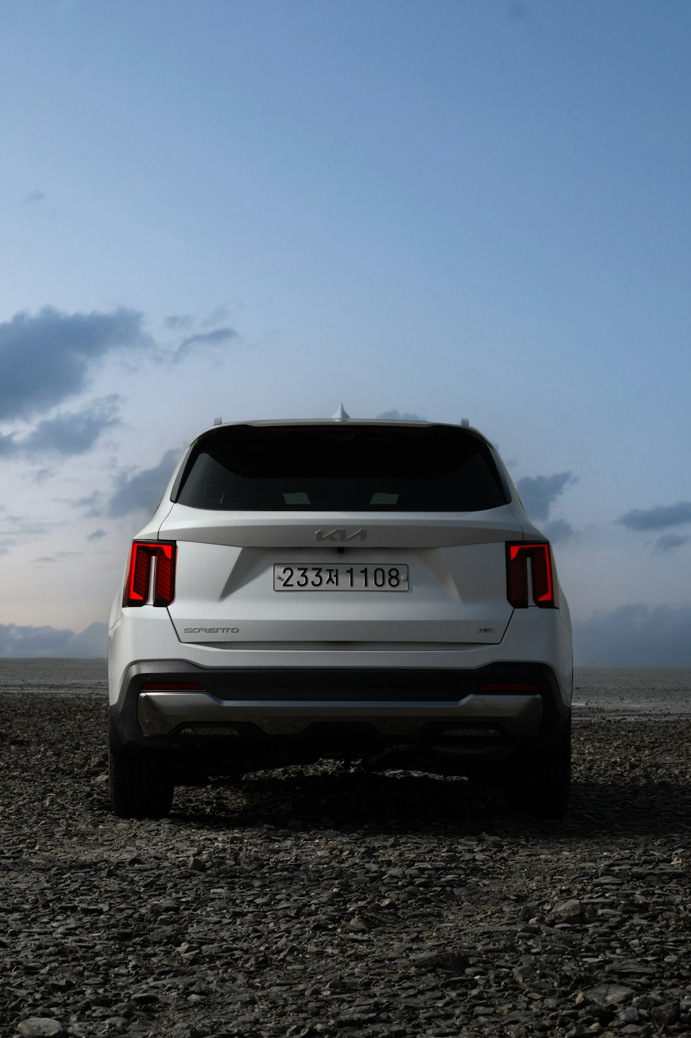 the back end of a white car parked on a rocky beach