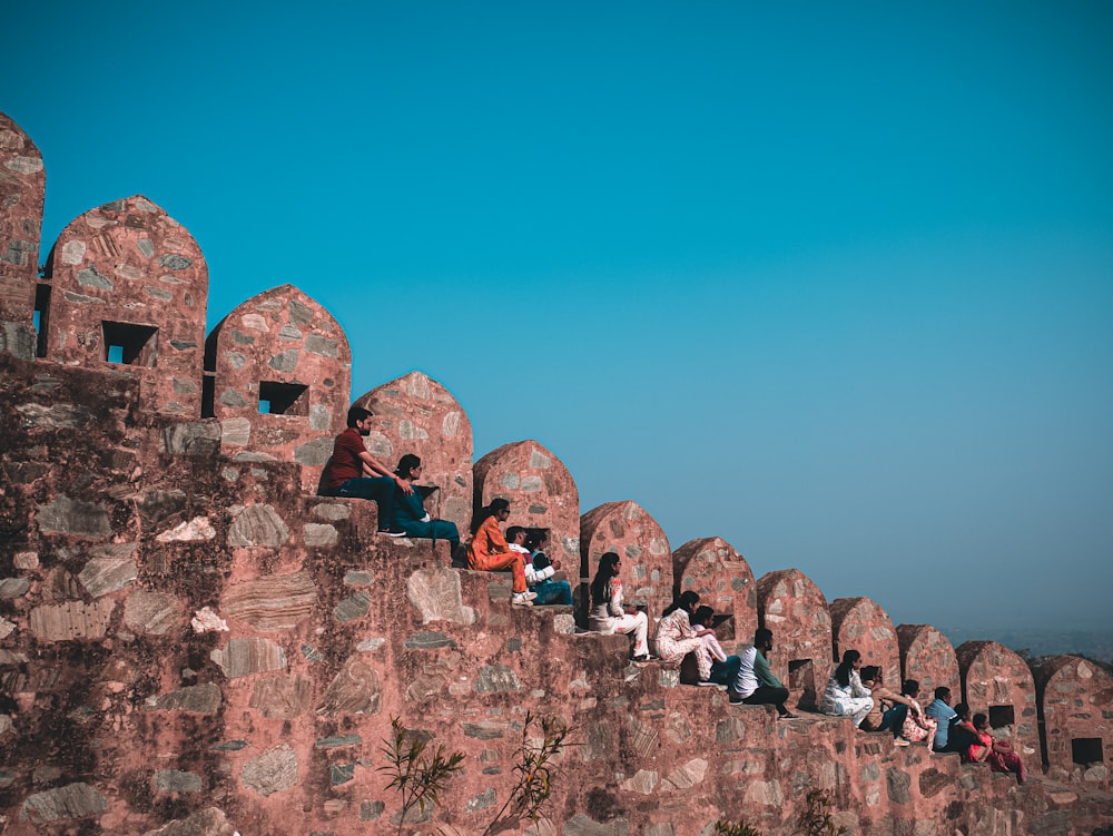 a group of people sitting on top of a stone wall