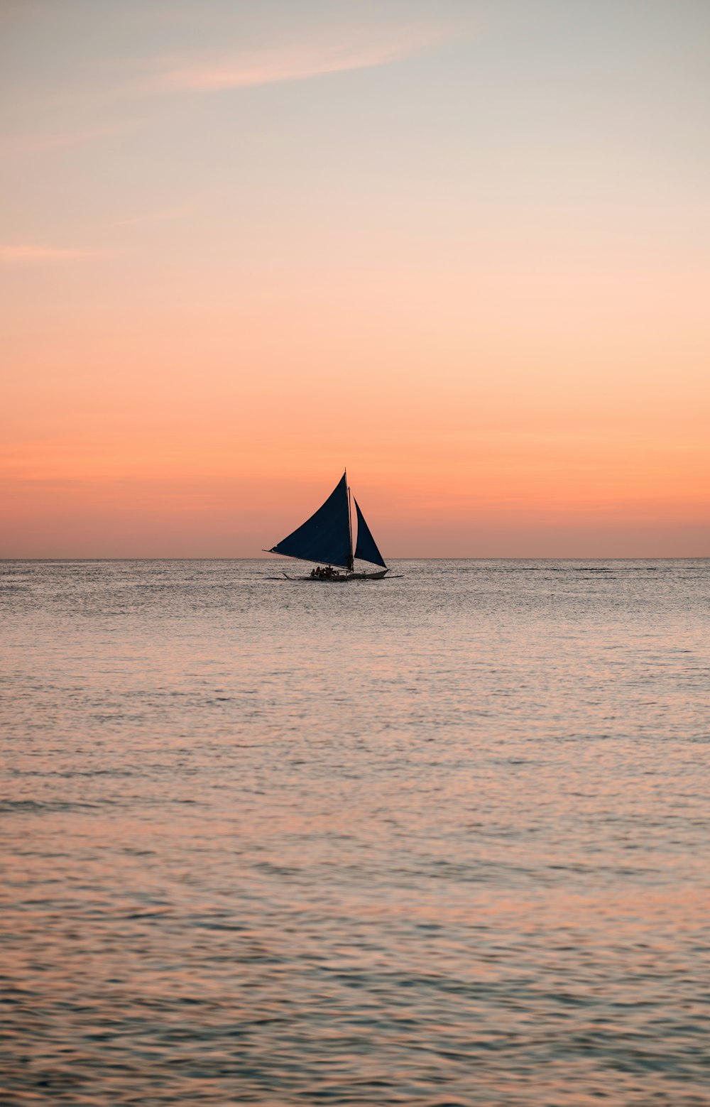 um veleiro no meio do oceano ao pôr do sol
