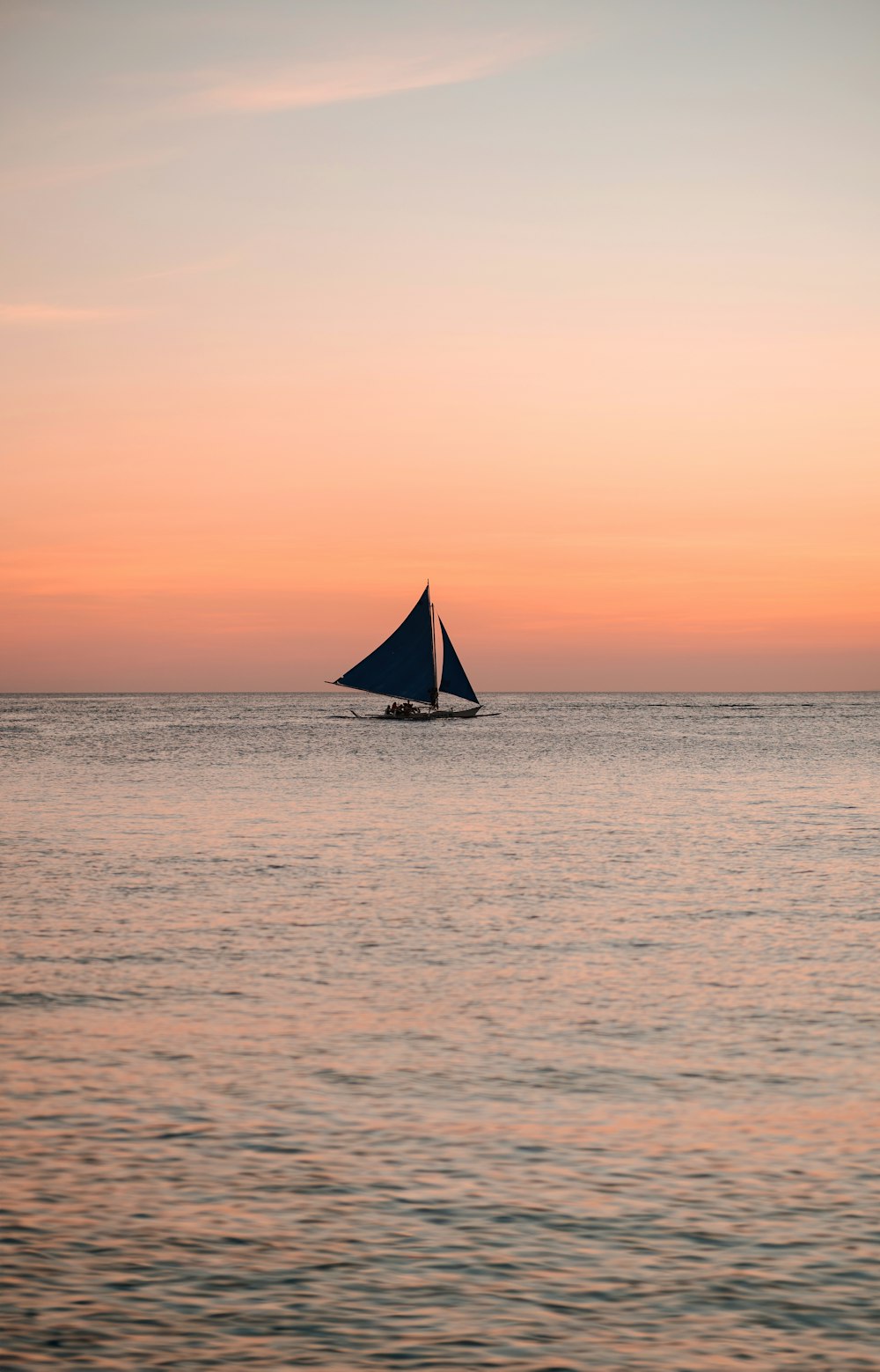 a sailboat in the middle of the ocean at sunset