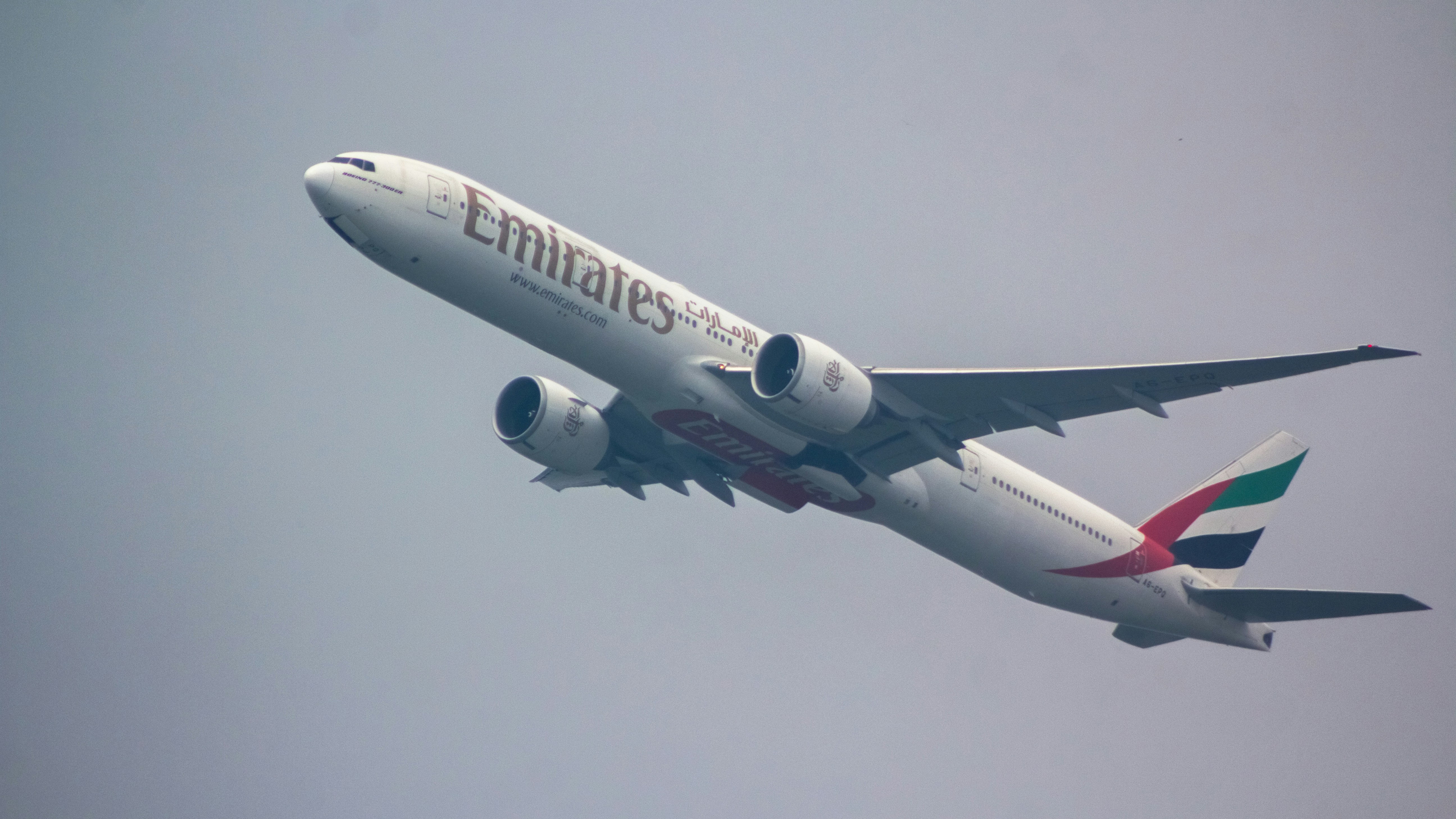 a large jetliner flying through a blue sky, Emirates Boeing 777