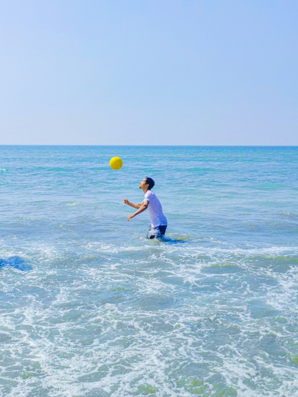 a man playing with a yellow ball in the ocean