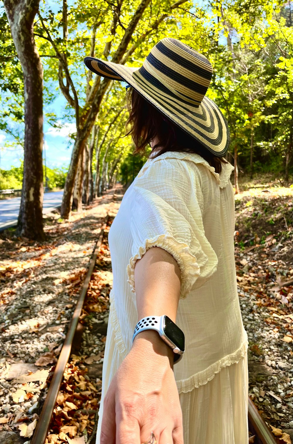 a woman in a dress and hat walking on a train track