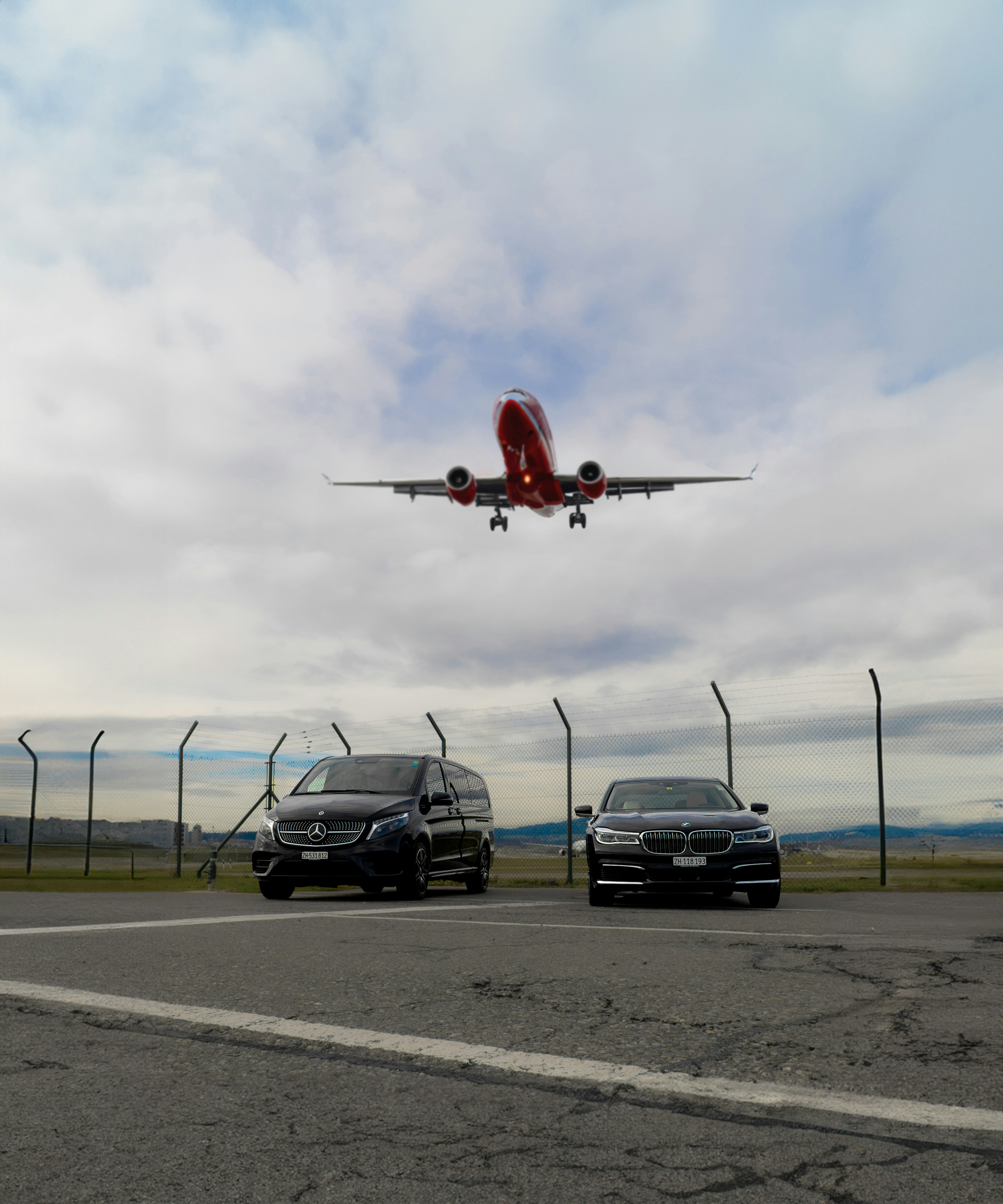 a large jet flying over two cars in a parking lot