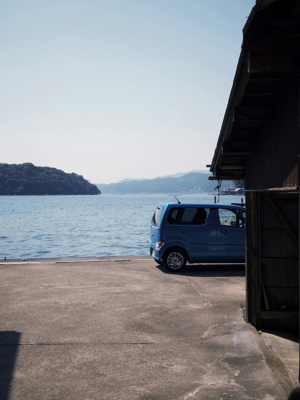 a small blue van parked next to a large body of water