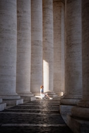 a woman sitting on the ground in front of a row of columns