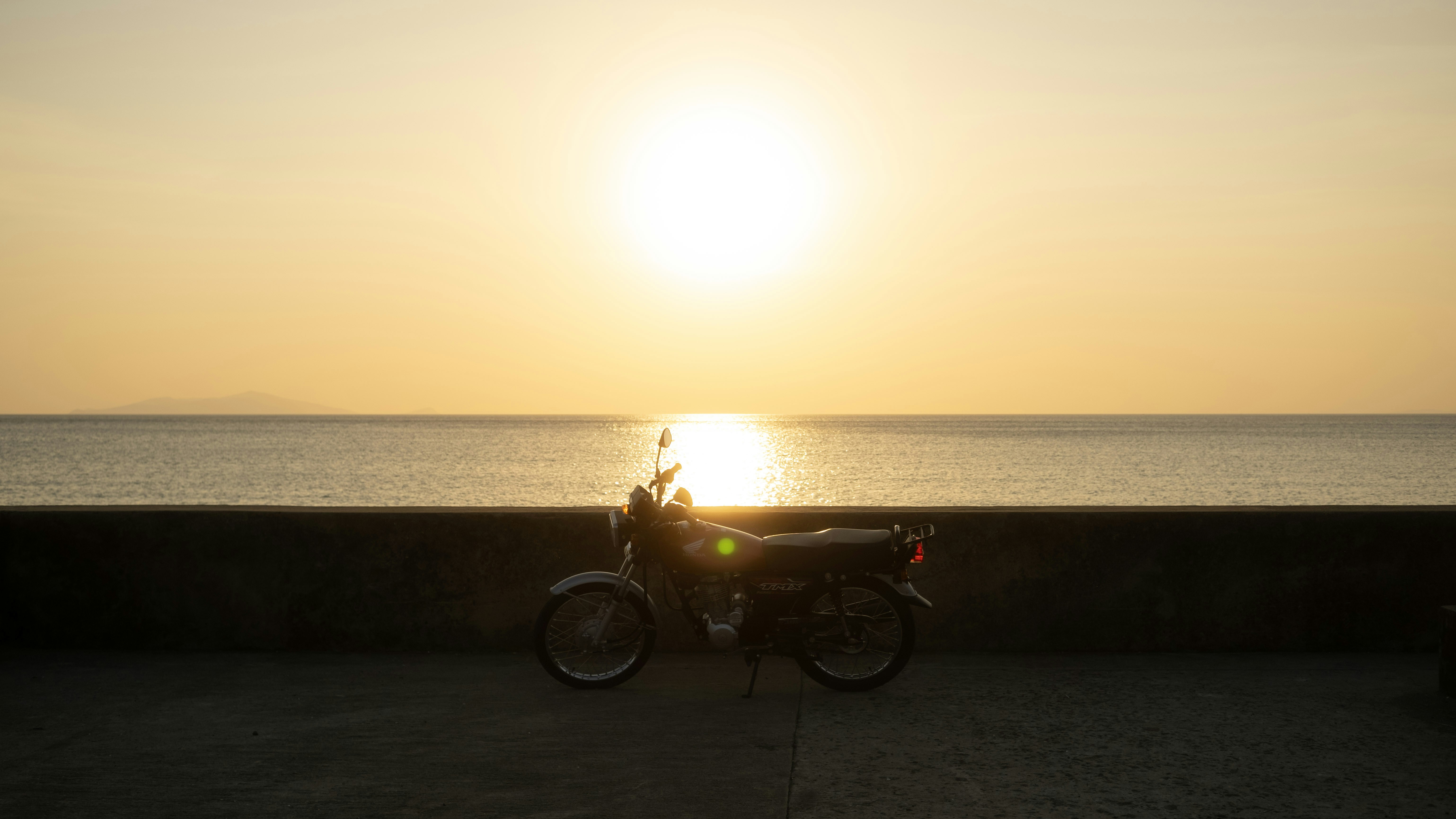 Pacific Coast Highway winding along dramatic California cliffs, turquoise ocean below, golden hour light, motorcycle silhouette