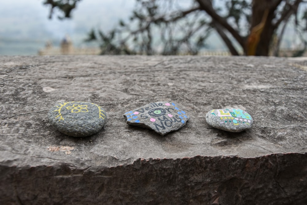 three painted rocks sitting on top of a rock