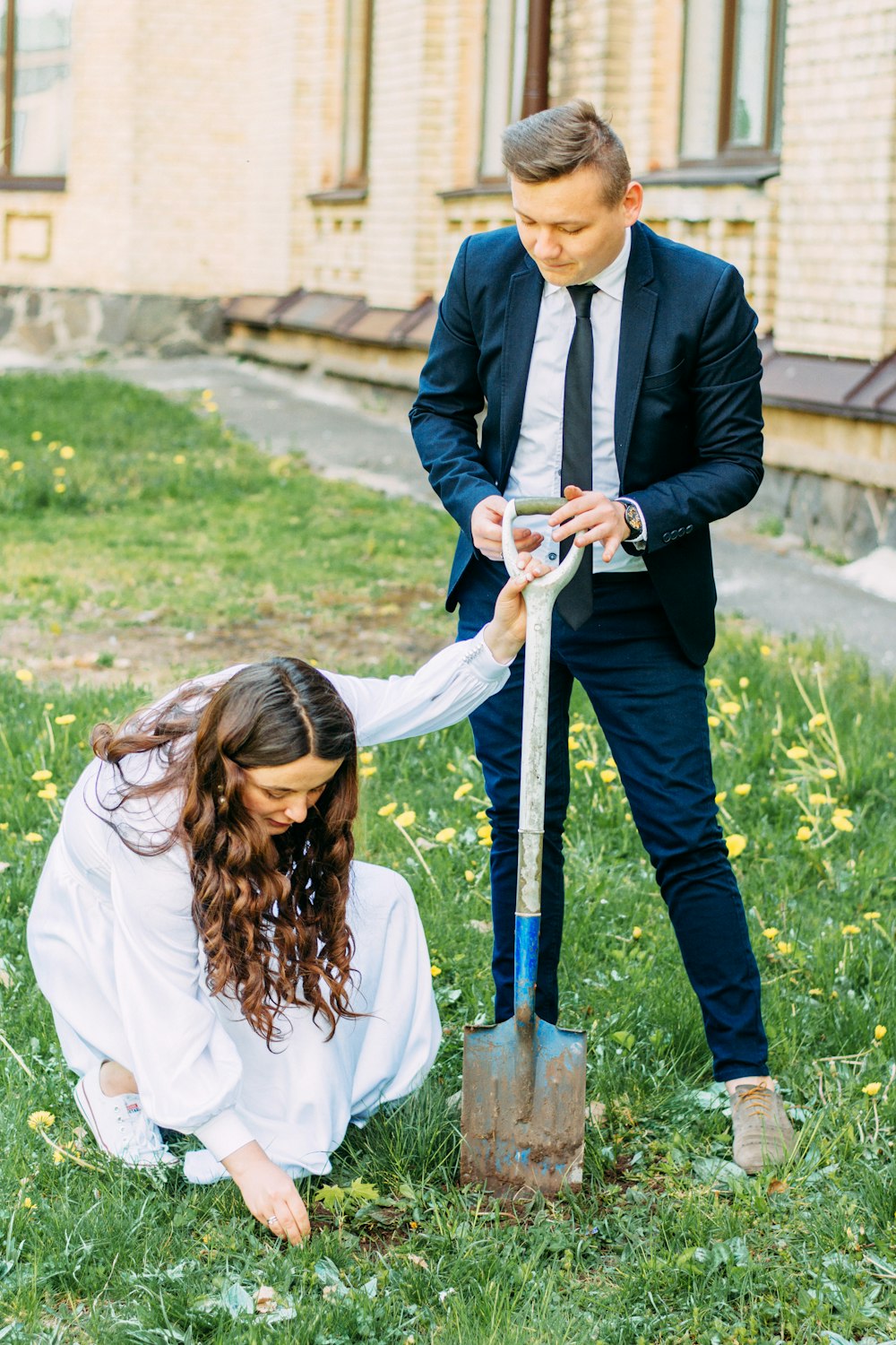 a man and a woman holding a shovel in the grass