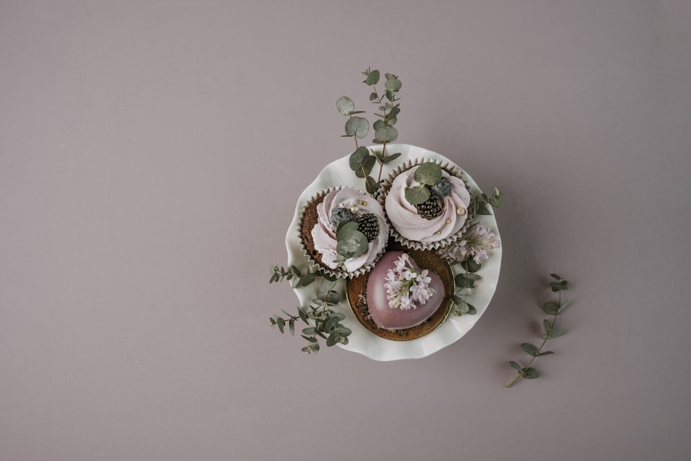 a plate of cupcakes with pink frosting and greenery