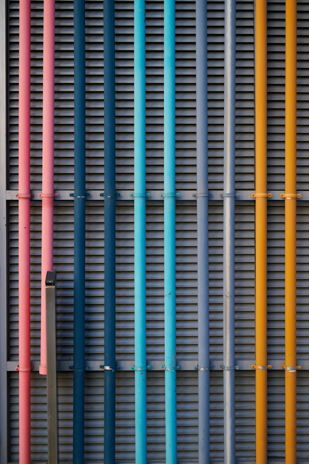 a row of multicolored metal pipes next to a building