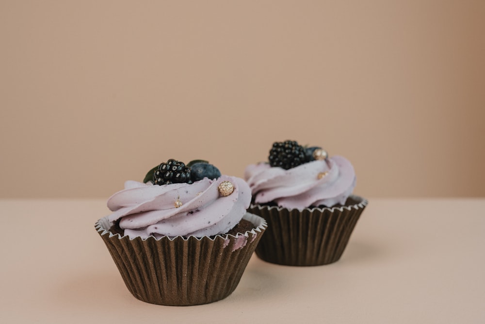 two cupcakes with white frosting and blackberries on top
