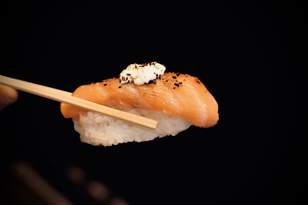 a person holding a piece of sushi with chopsticks