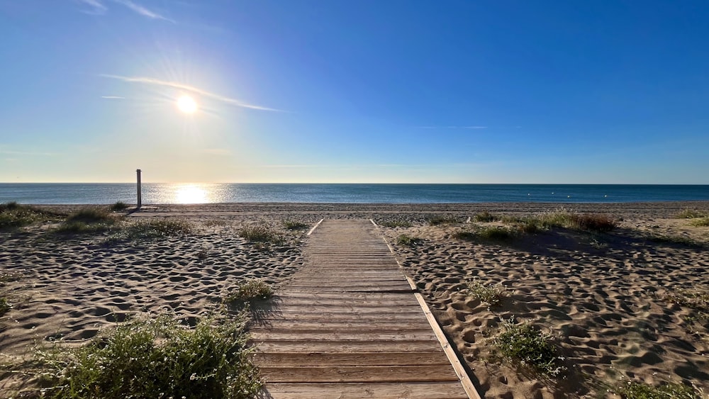 a wooden walkway leading to the beach with the sun in the background