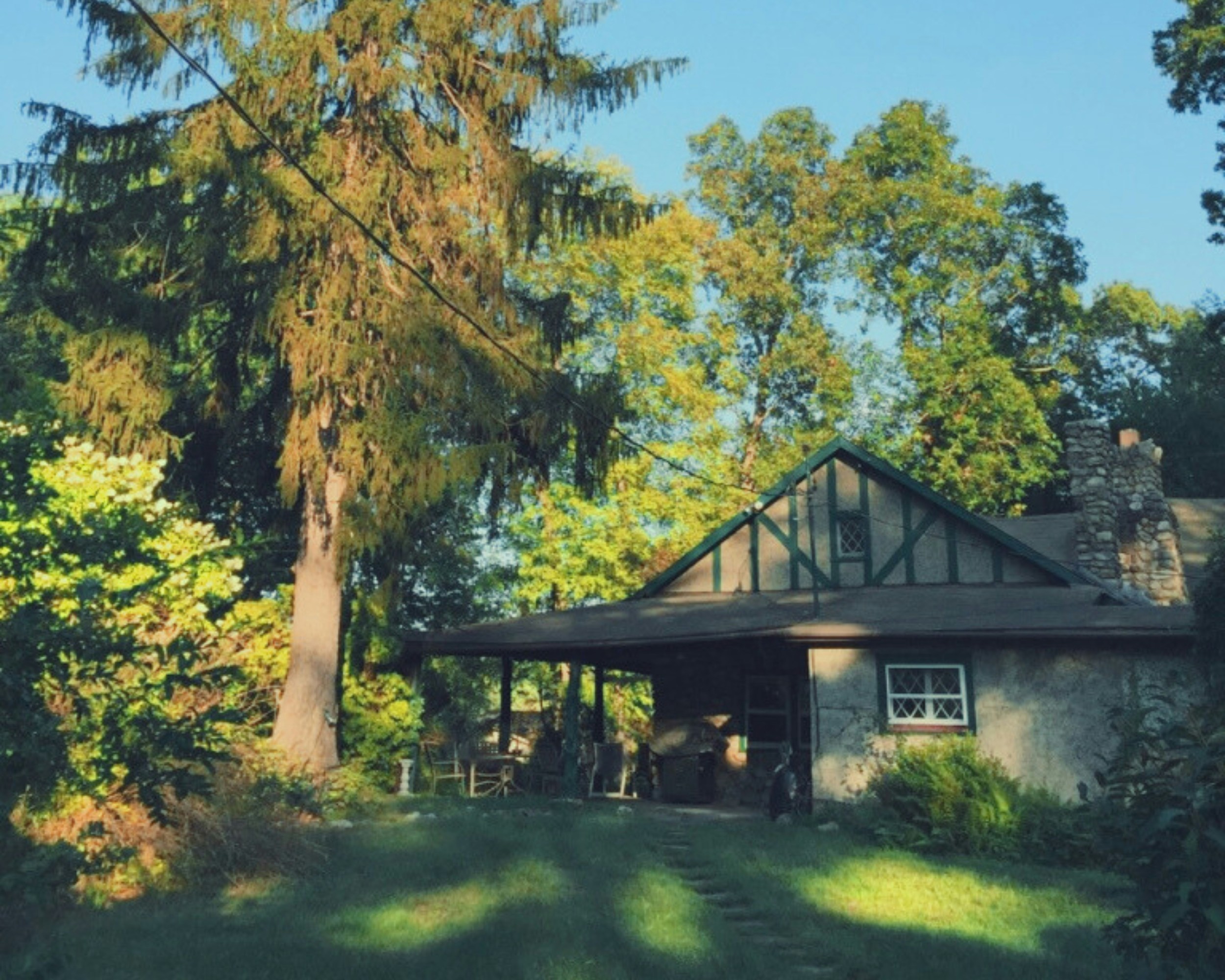 Cozy cottage-style home with covered porch, flower garden, and warm afternoon light filtering through trees