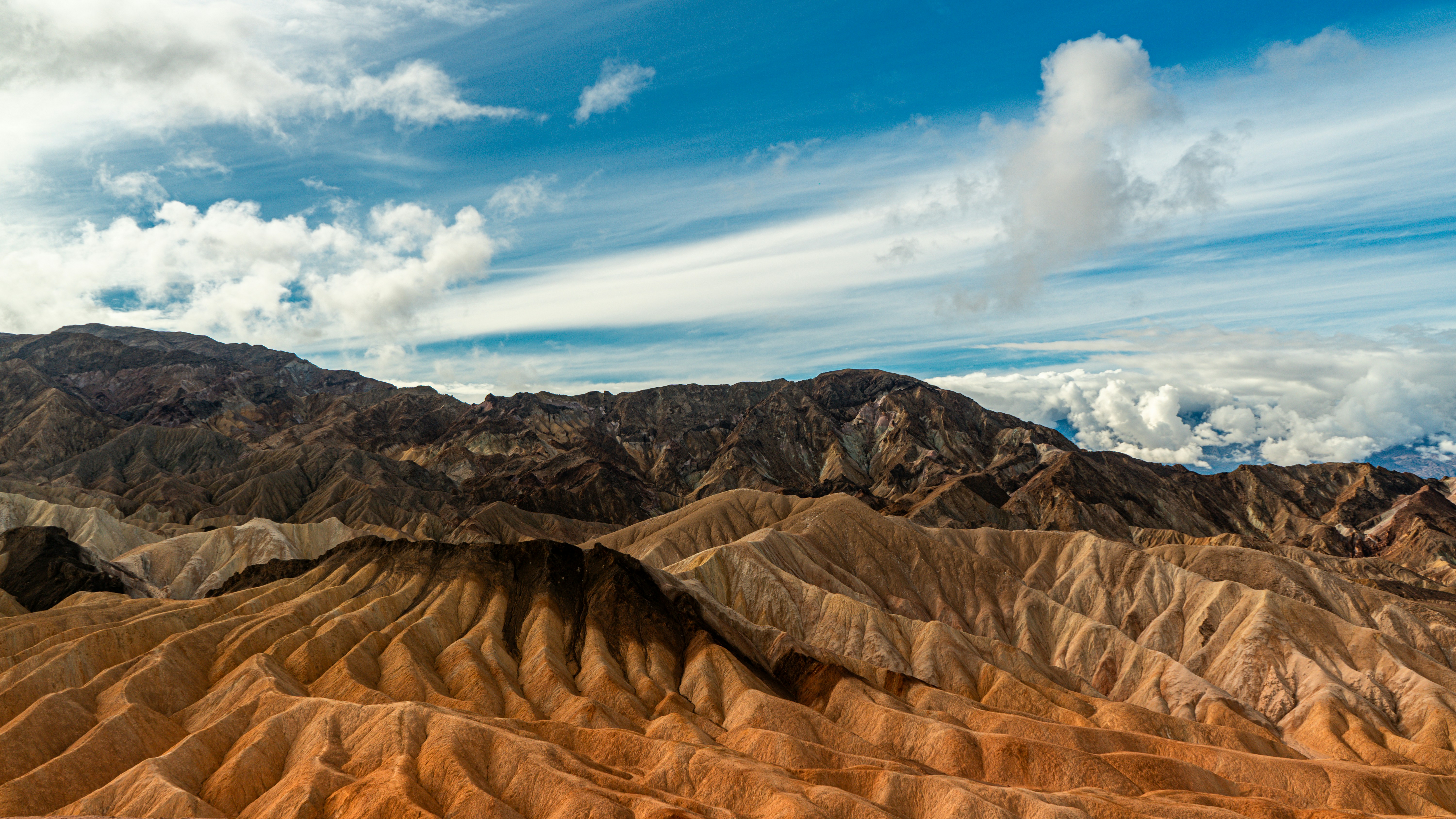 a view of a mountain range in the desert, The view at Zabriskie point, mountains and sky sweeping up in the distance.