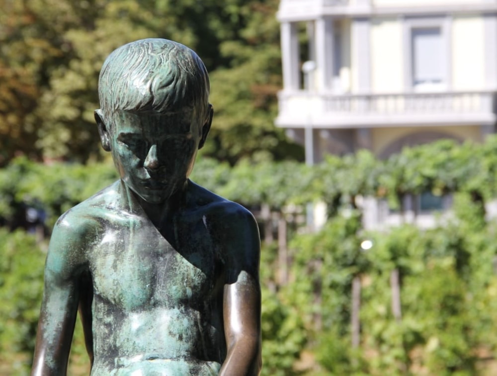 a bronze statue of a boy in front of a house