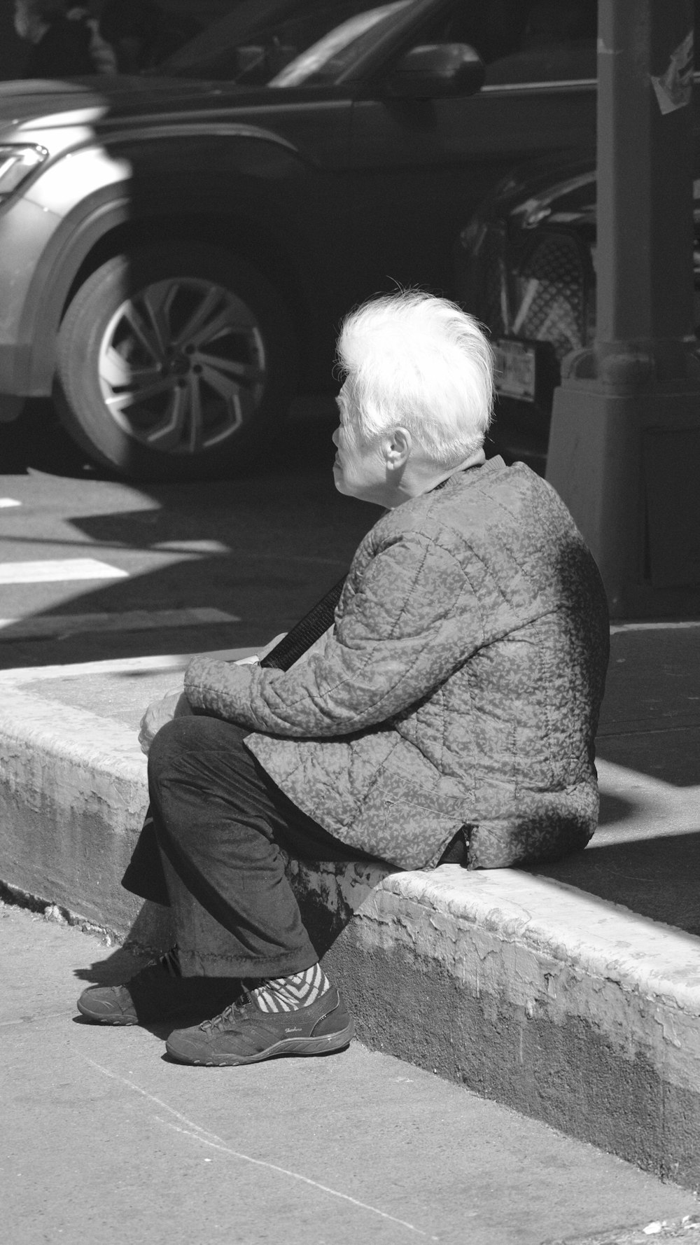 a black and white photo of a person sitting on a curb