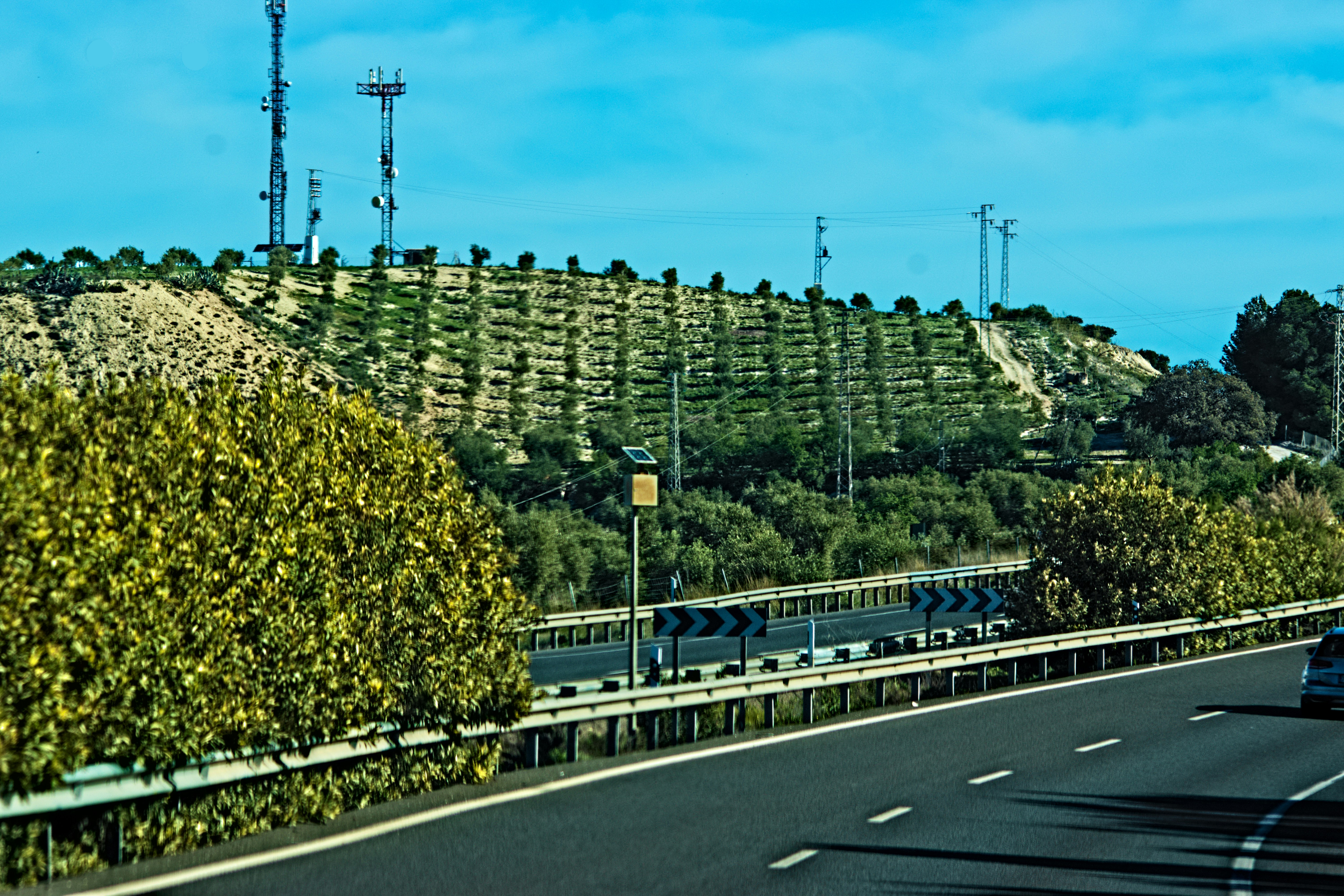 a car driving down a road next to a lush green hillside