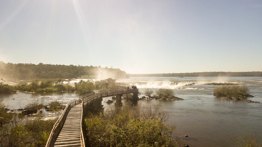 a wooden bridge over a river with a waterfall in the background