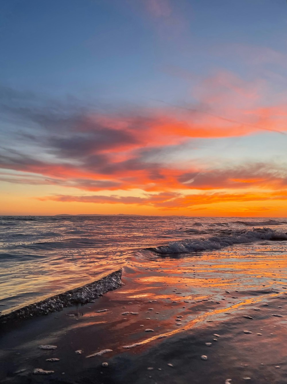 a sunset over the ocean with waves crashing on the shore