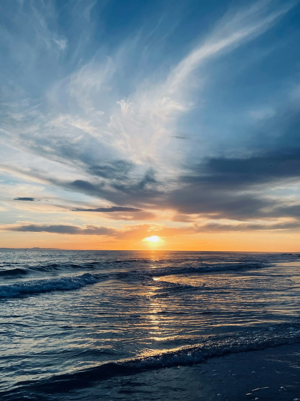 the sun is setting over the ocean on a cloudy day