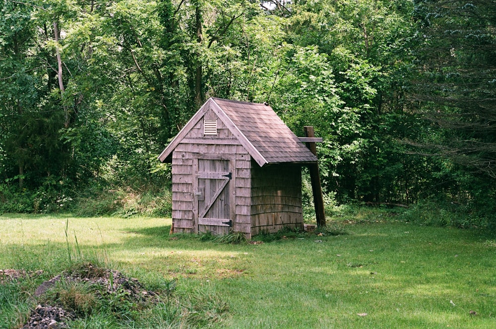 a small wooden outhouse in the middle of a field