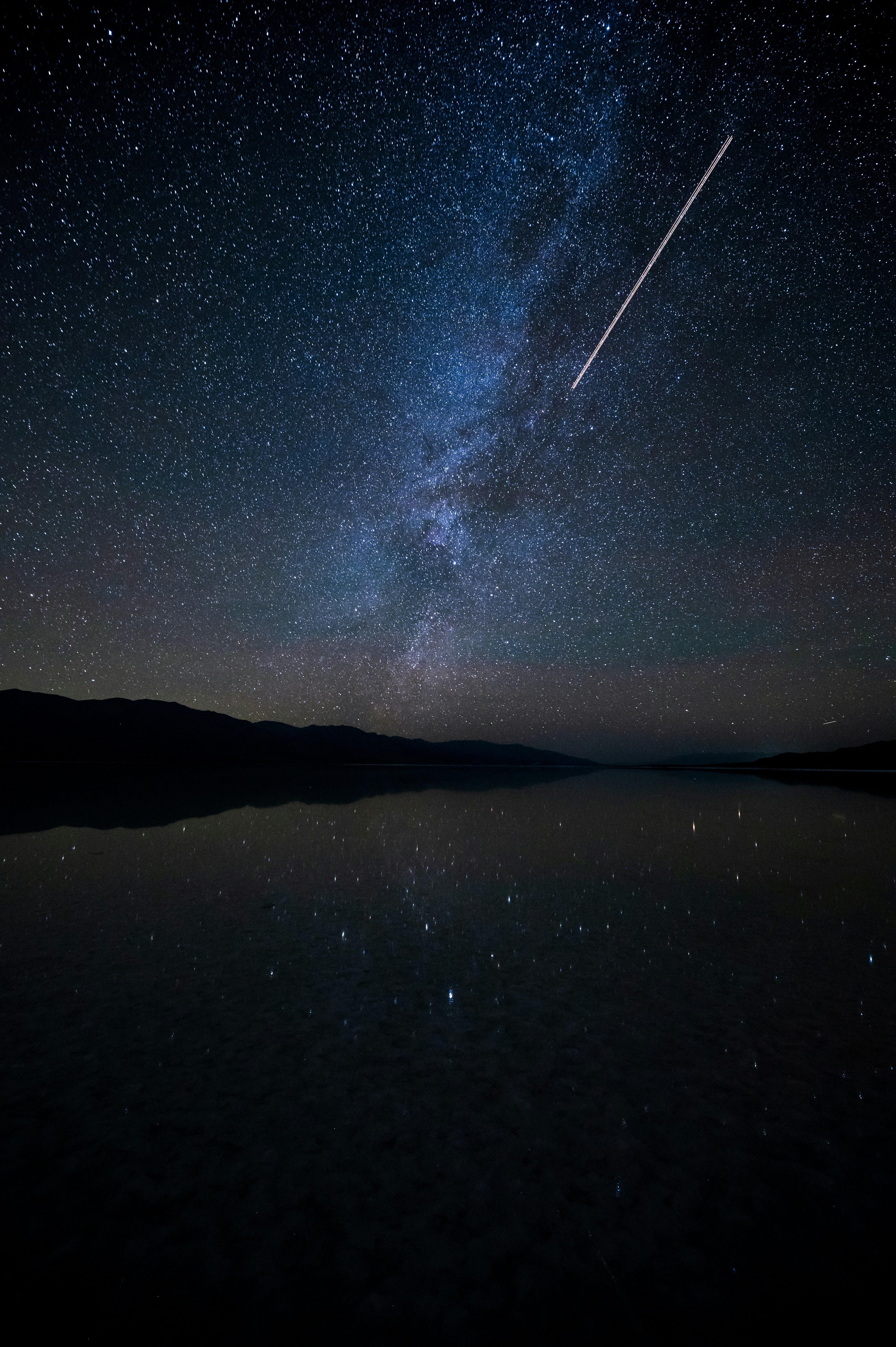 Milky Way galaxy arch reflected perfectly in a calm mountain lake, symmetrical reflection in dark still water