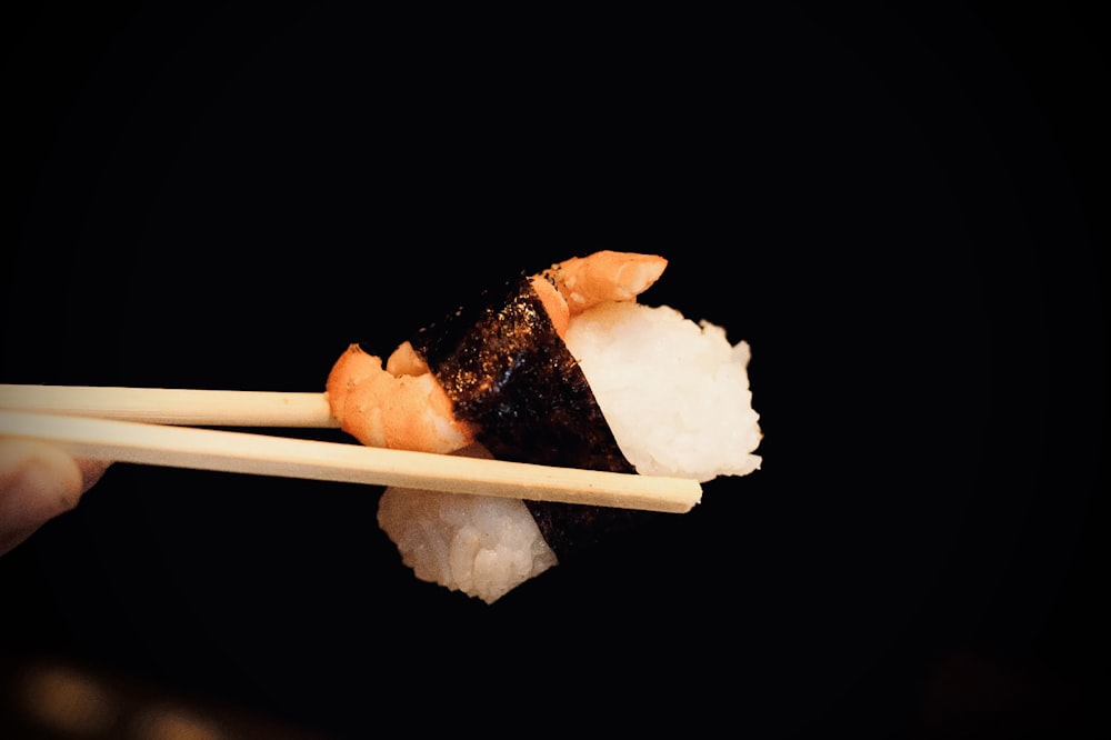 a person holding a piece of sushi with chopsticks