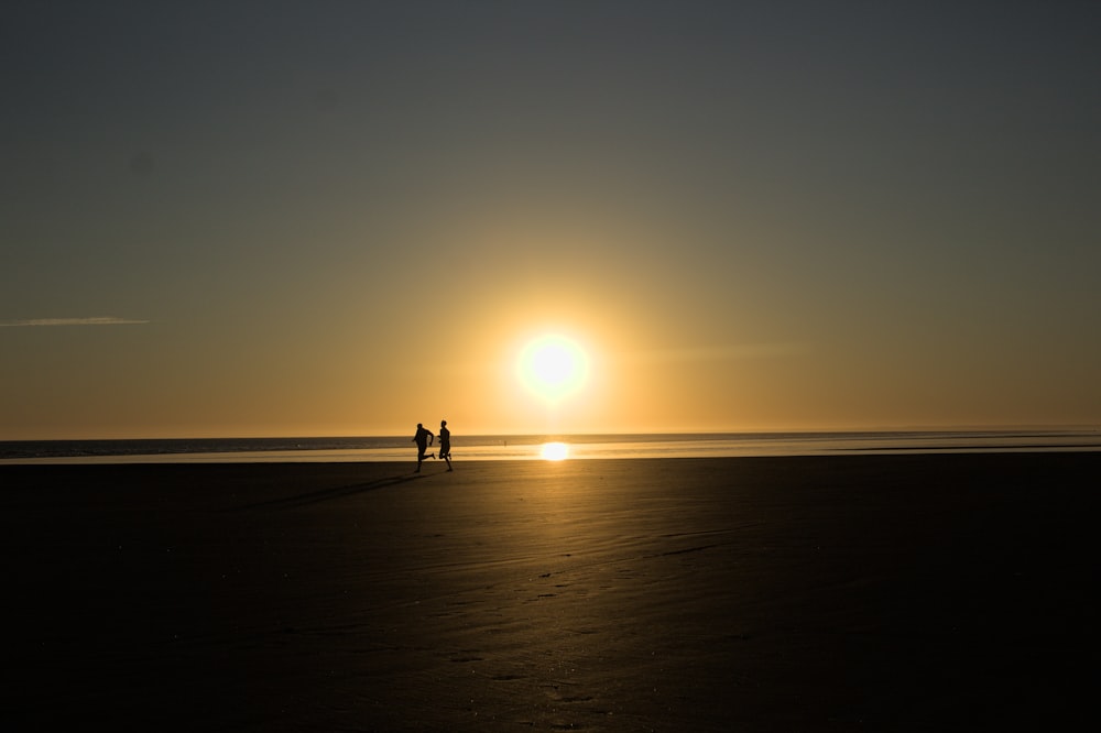 a couple of people standing on top of a sandy beach