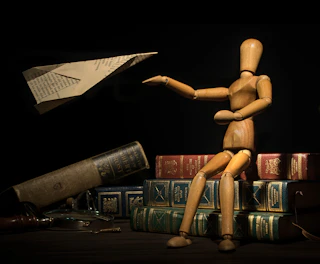 a wooden doll sitting on top of a pile of books