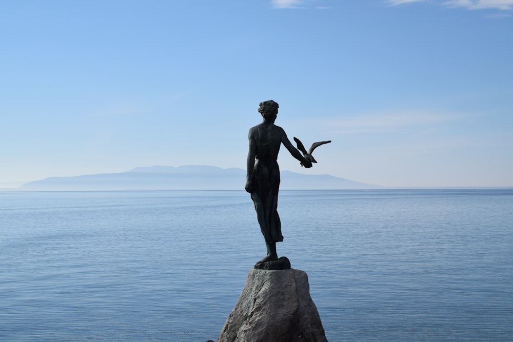 a statue of a woman holding a bird on top of a rock