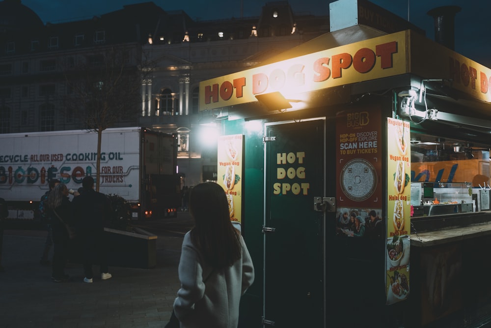 a woman standing outside of a hot dog stand at night