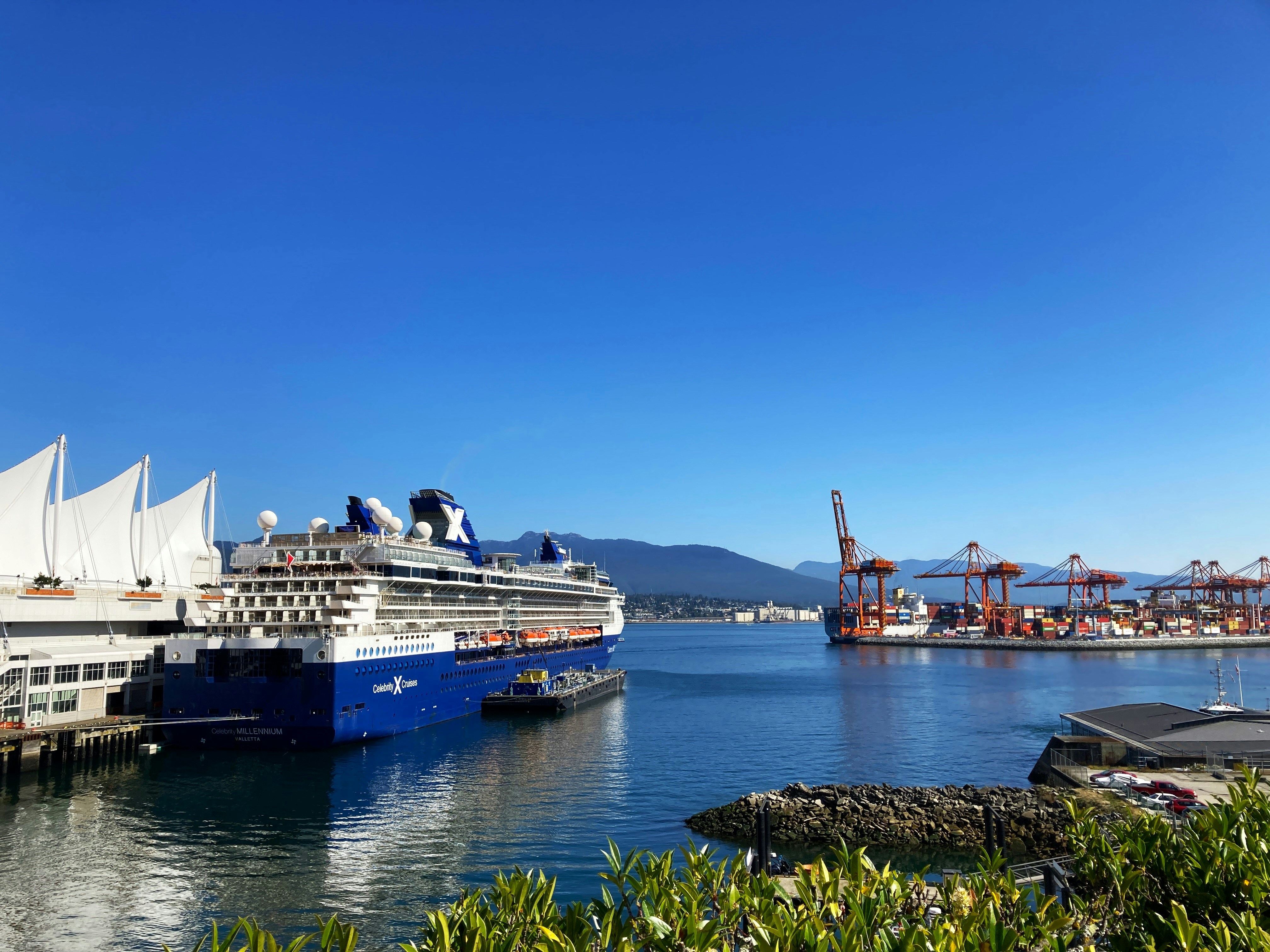 A Celebrity cruise ship lies at the Canada Place terminal with the port cranes and North Shore mountains beyond.