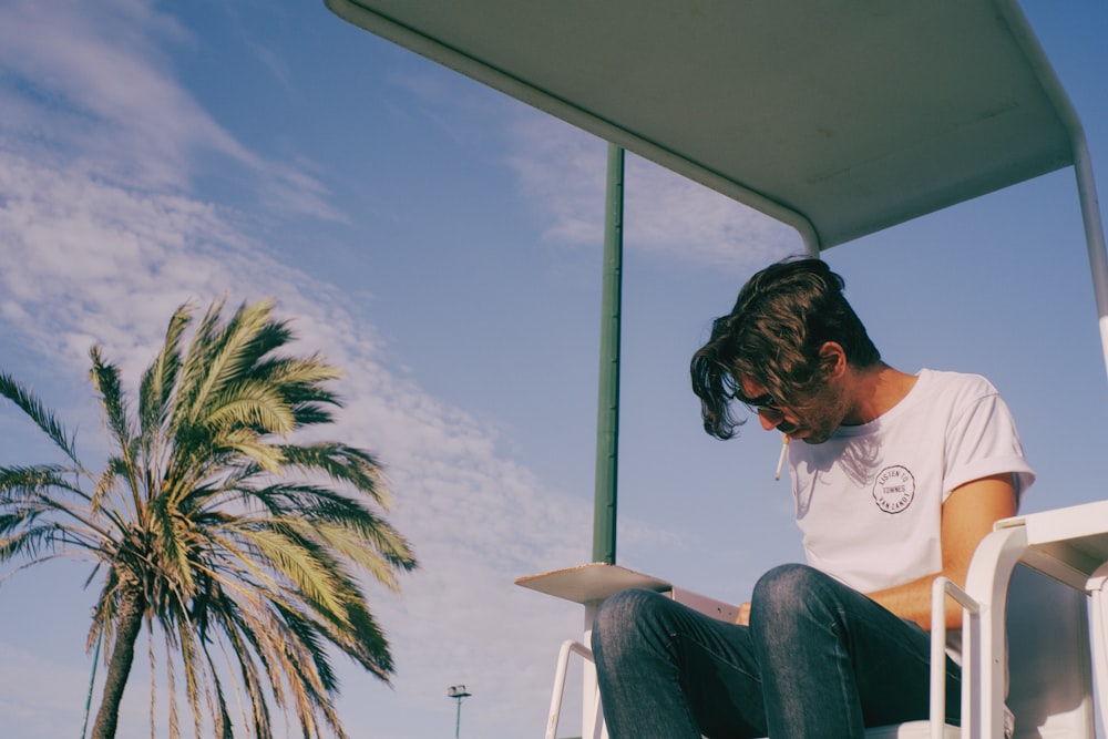 a man sitting on a chair next to a palm tree