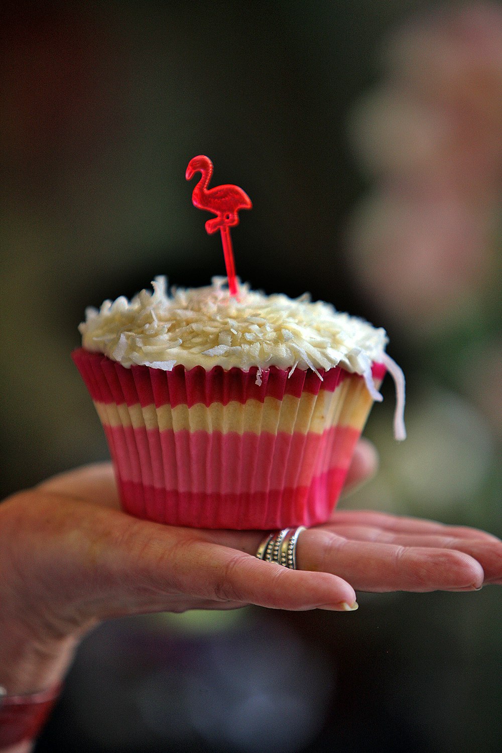 a person holding a cupcake with a flamingo candle on top