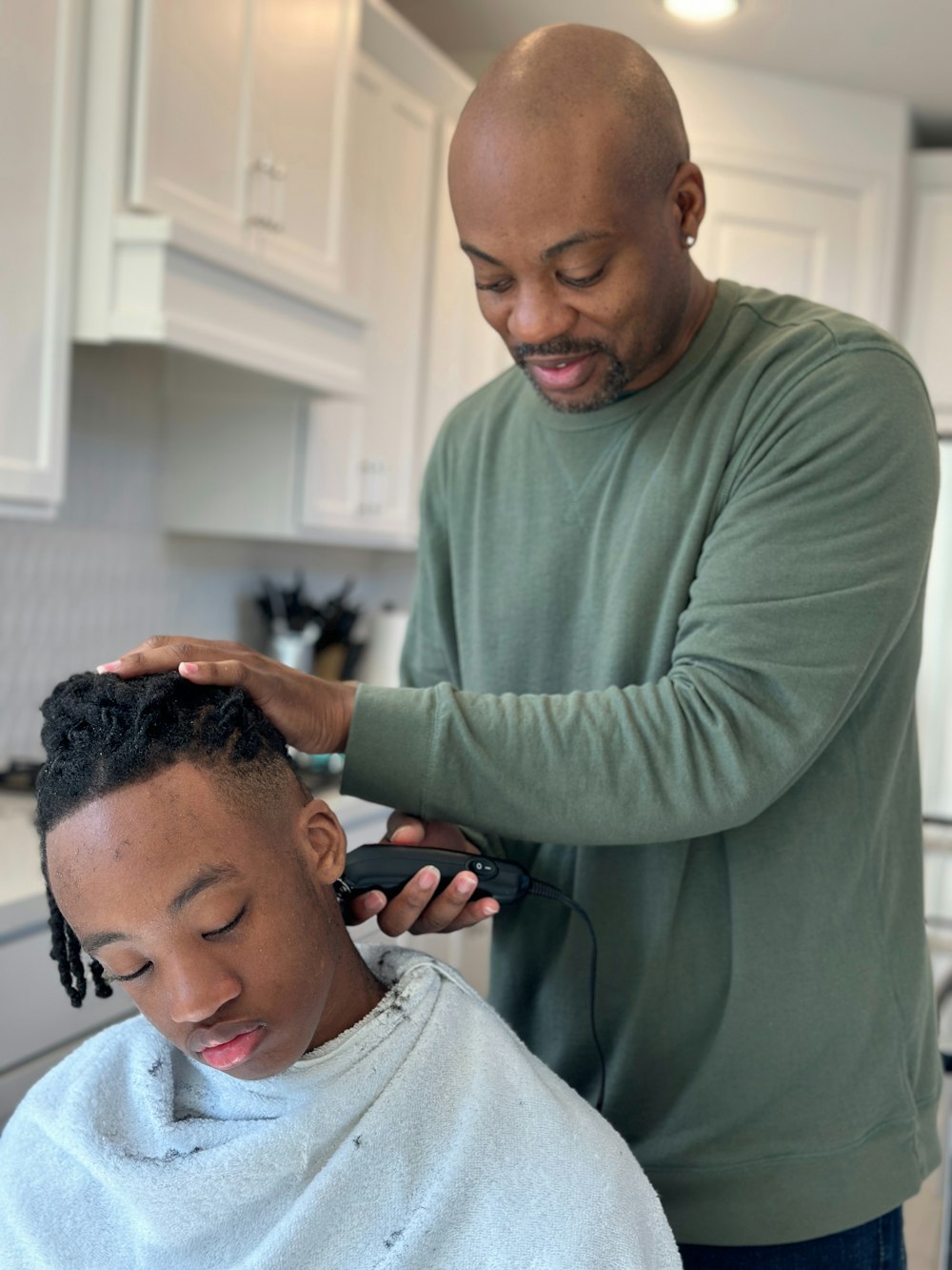 a man cutting another mans hair in a kitchen