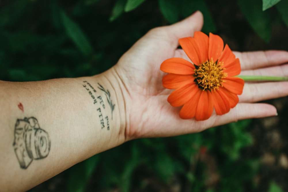 Der Arm einer Person mit einer Tätowierung, die eine Blume hält