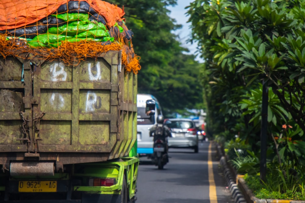 a green truck driving down a street next to a lush green forest