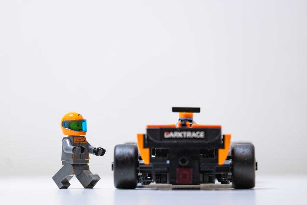 a lego man walking next to a lego race car