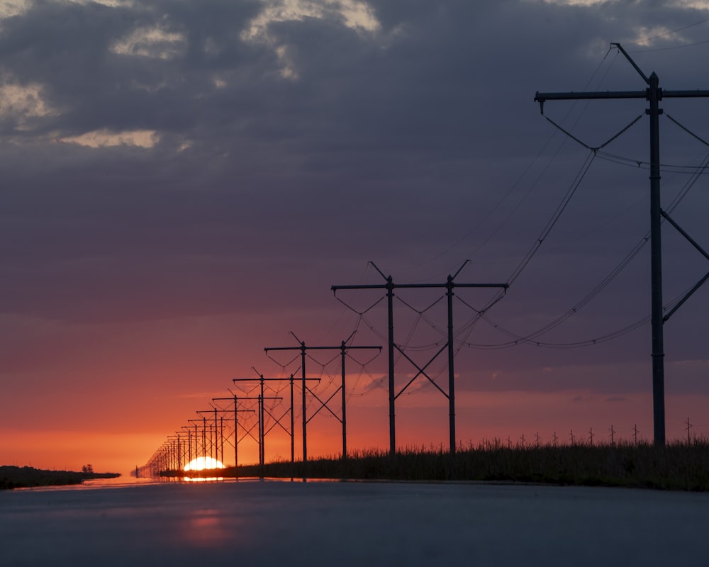 the sun is setting behind a line of power poles