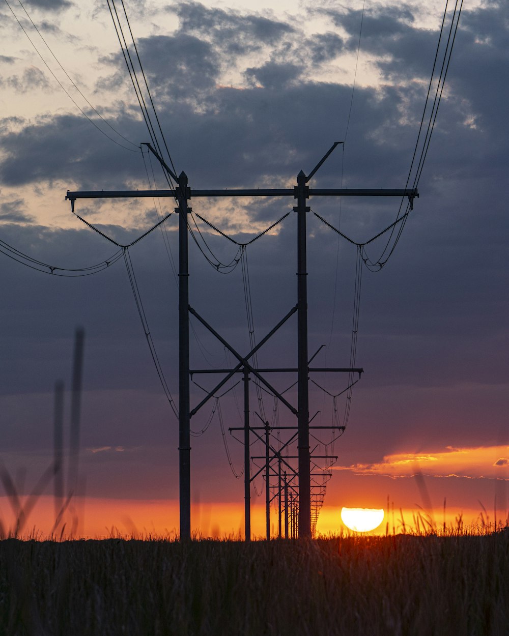 the sun is setting behind power lines in a field