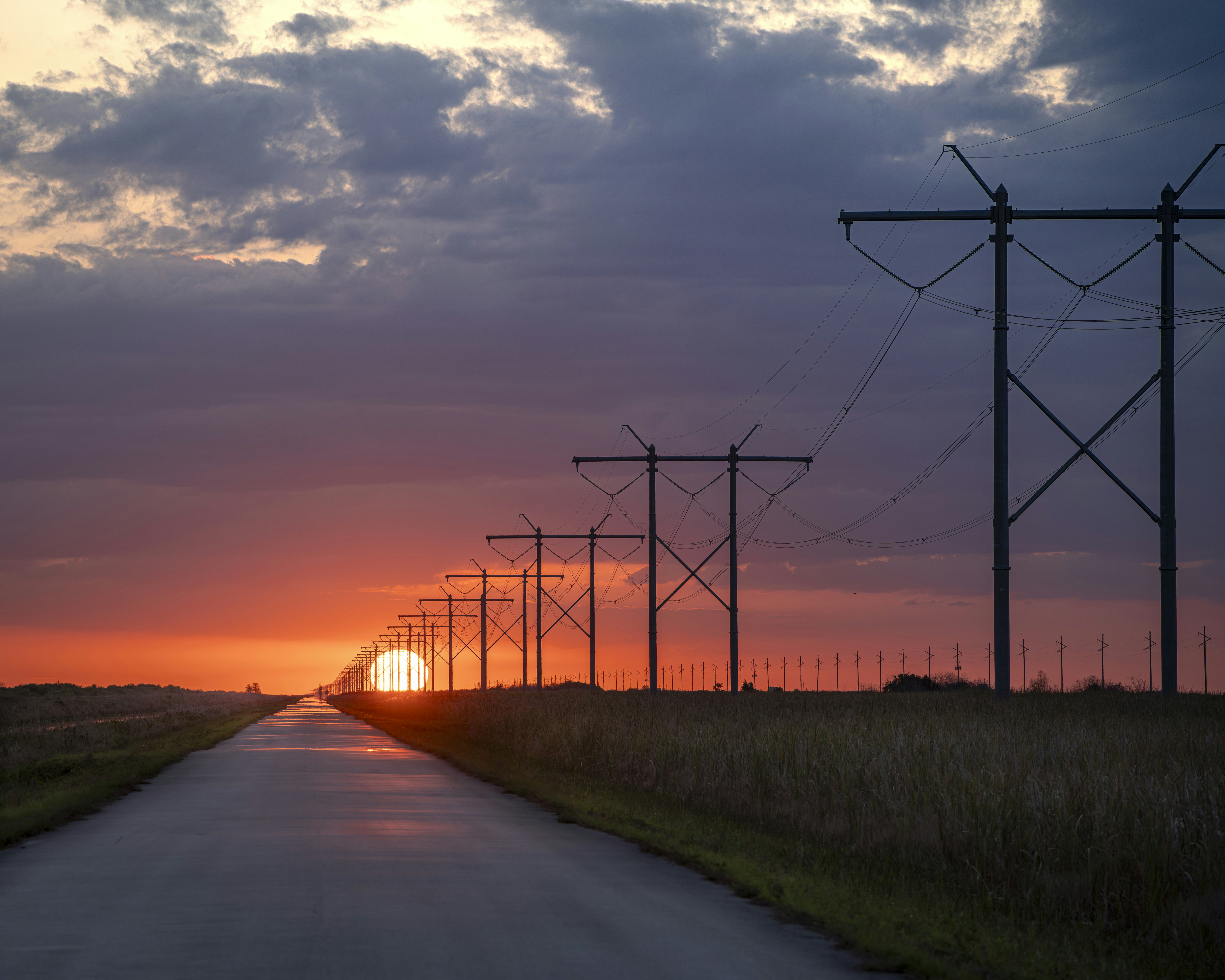 the sun is setting behind a line of power poles