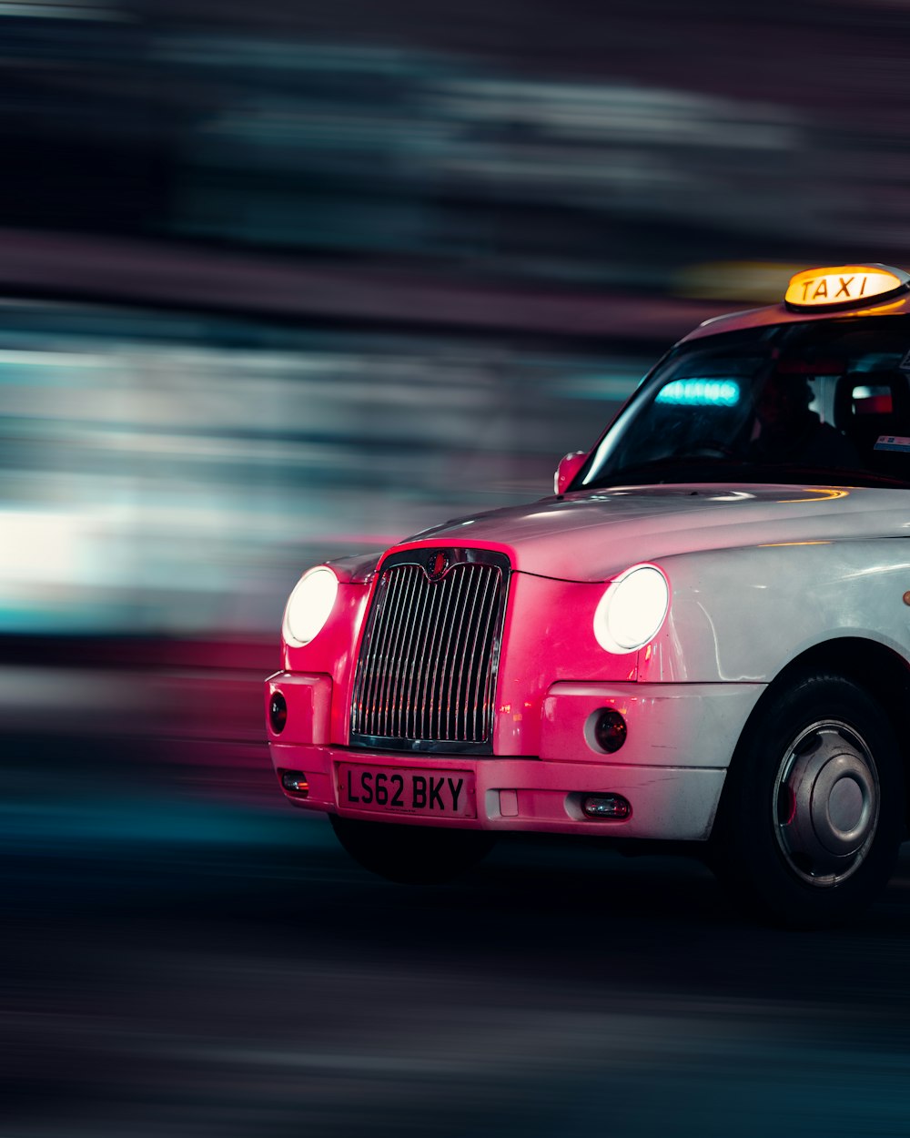 a white taxi cab driving down a street at night